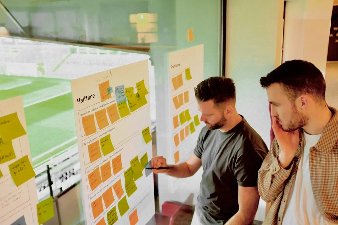 Twee mensen bekijken een bord vol post-its tijdens een workshop